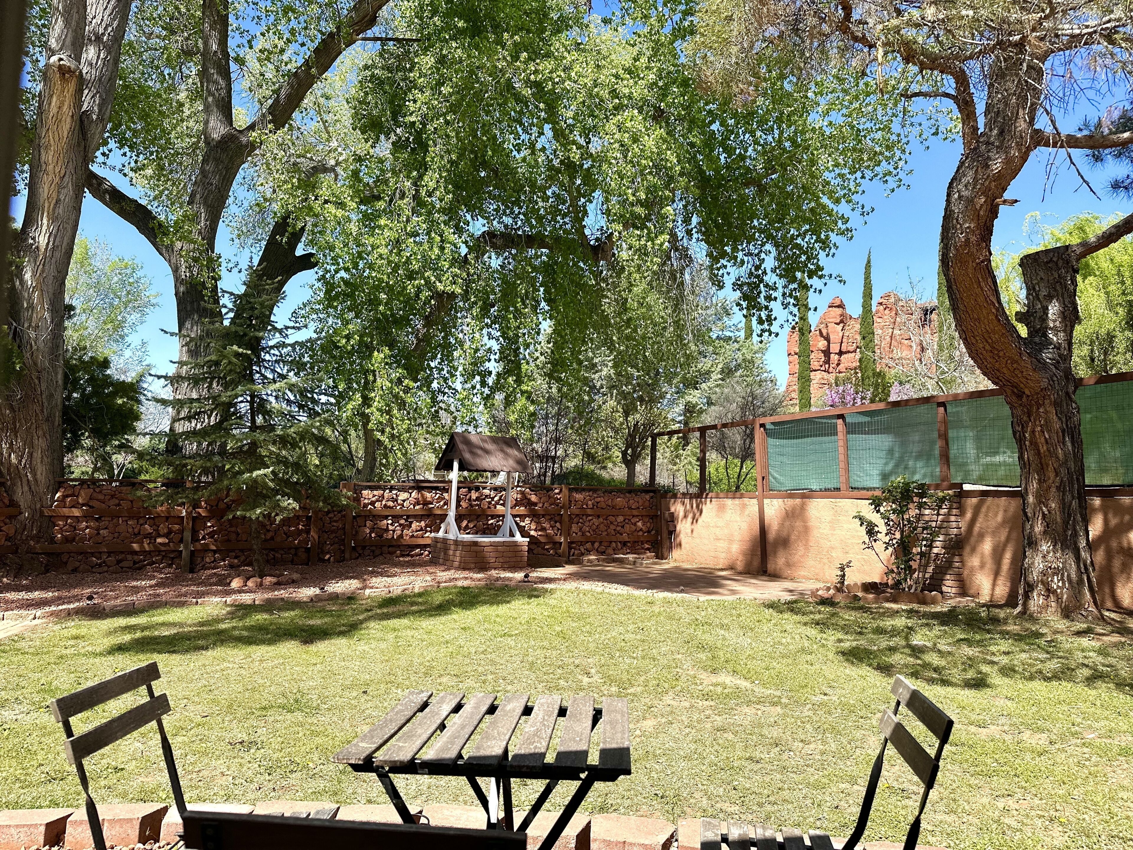 Un área de picnic con una mesa y bancos de madera, rodeada de árboles y un muro de piedra.