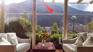 A balcony with two white sofas, a wooden table with a vase of flowers, and a view of a cityscape and mountains. - Jindu Hotel (Longnan)