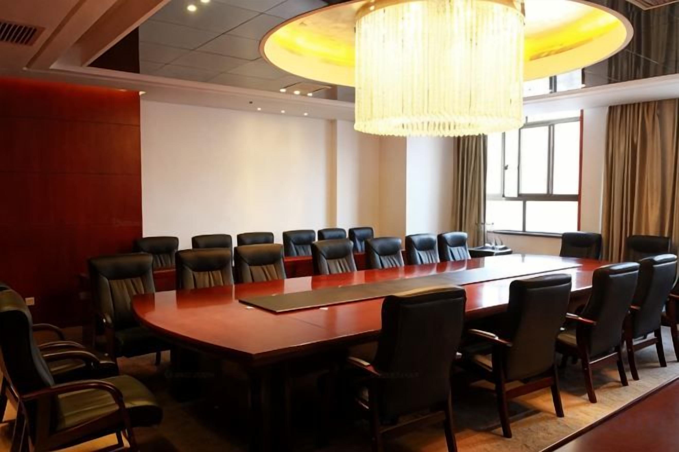 A conference room with a long table and multiple chairs, a chandelier, and a large window with curtains.