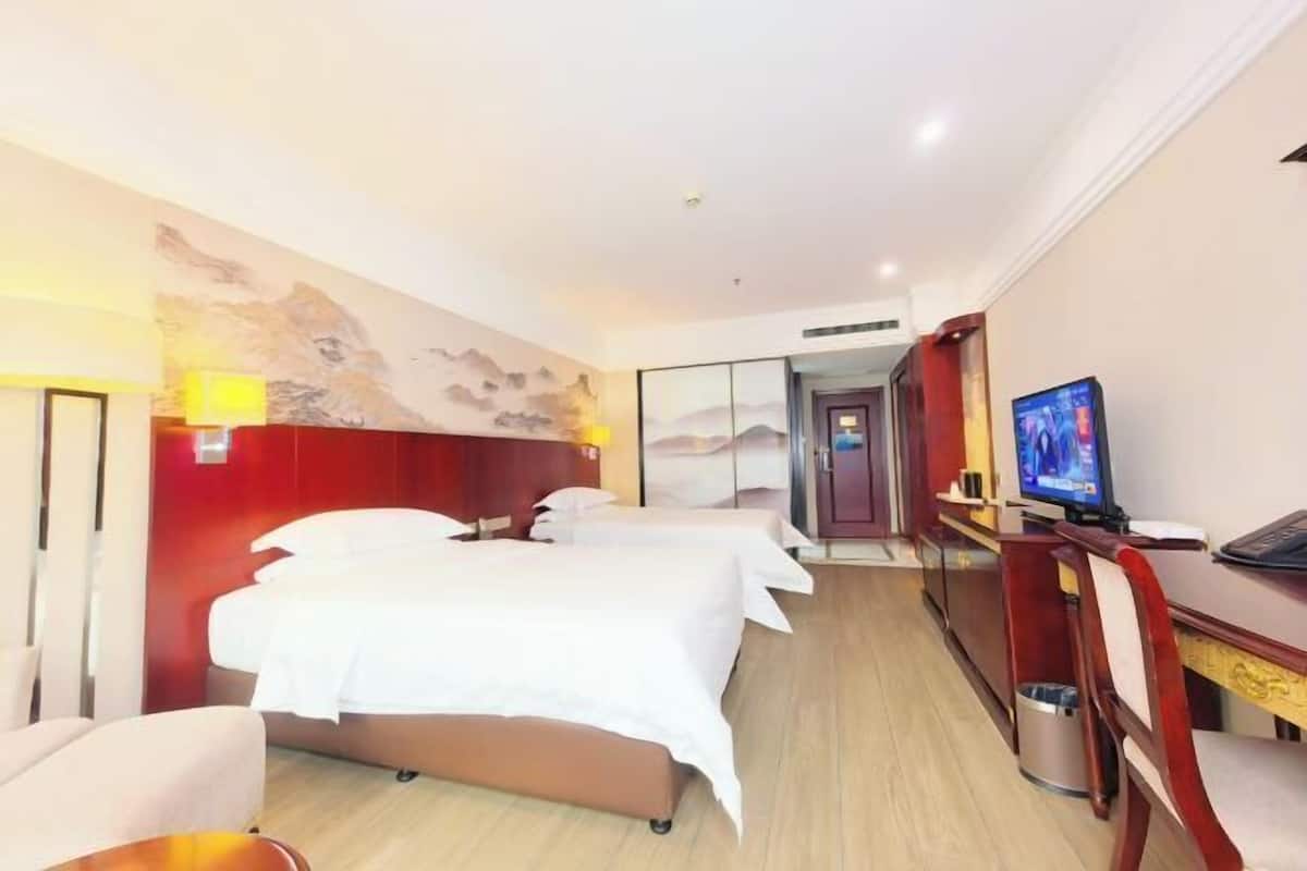 A hotel room with a bed, a desk, a television, and a wall with a painting.