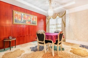 A dining area with a red wall, a large painting, a chandelier, and a table with chairs. - Jindu Hotel (Longnan)