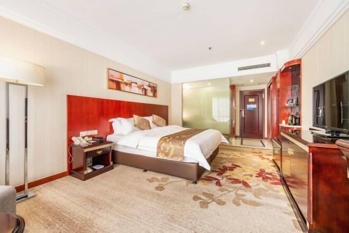 A hotel room with a large bed, a TV, a desk with a phone, and a carpeted floor.
