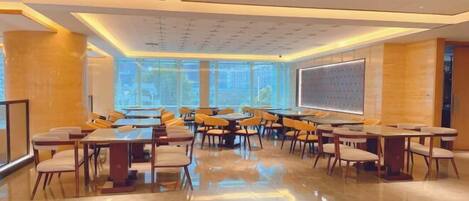 A spacious conference room with multiple tables and chairs, large windows, and a projection screen.