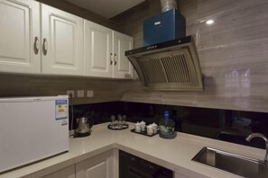 A kitchen with white cabinets, a stainless steel sink, a built-in range hood, and a refrigerator. - Jindu Hotel (Longnan)