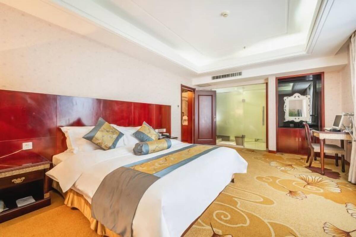 A hotel room with a large bed, a desk, and a mirror.