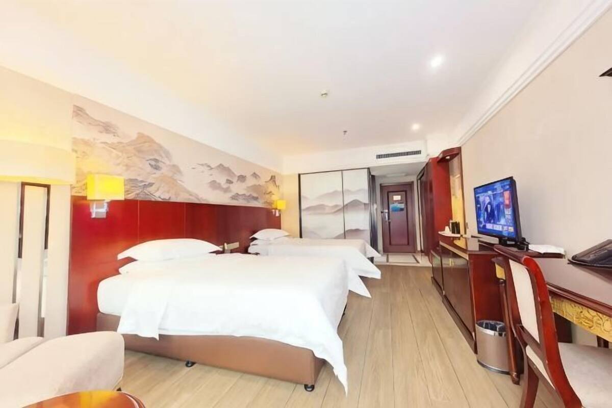 A hotel room with a bed, a desk, a television, and a wall with a painting.