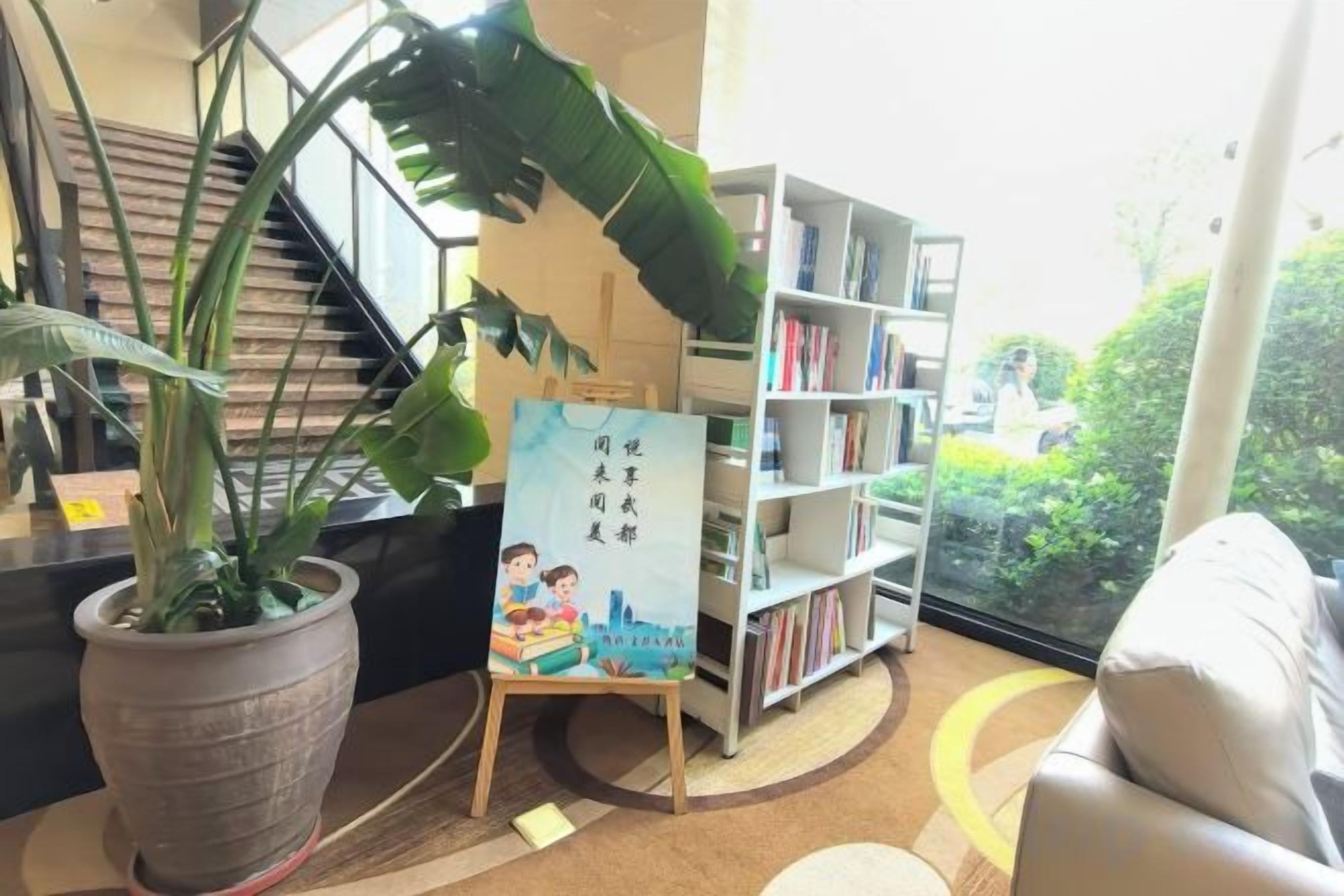 Un área de recepción con una escalera, una planta en maceta, una estantería y un cartel.