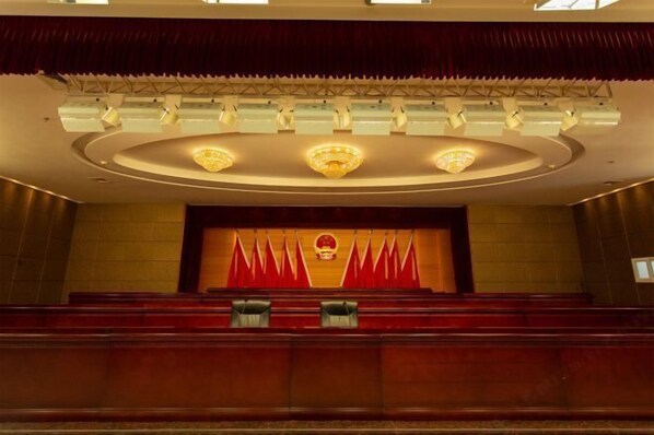A conference room with a stage, red curtains, and a chandelier.