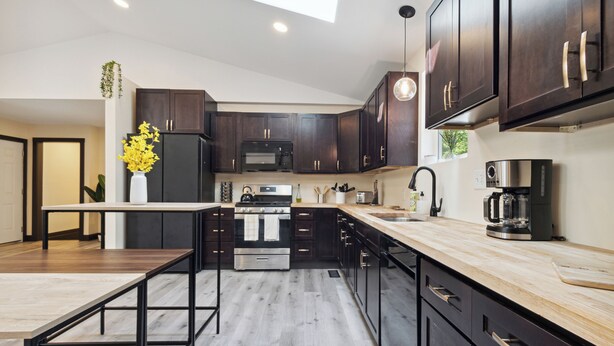 A modern kitchen with dark wood cabinets, a central island, stainless steel appliances, and a skylight. - Emerald in Berkeley Springs, WV (Berkeley Springs)