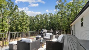 An outdoor deck with wicker furniture, a grill, and a view of a forested area. - Emerald in Berkeley Springs, WV (Berkeley Springs)