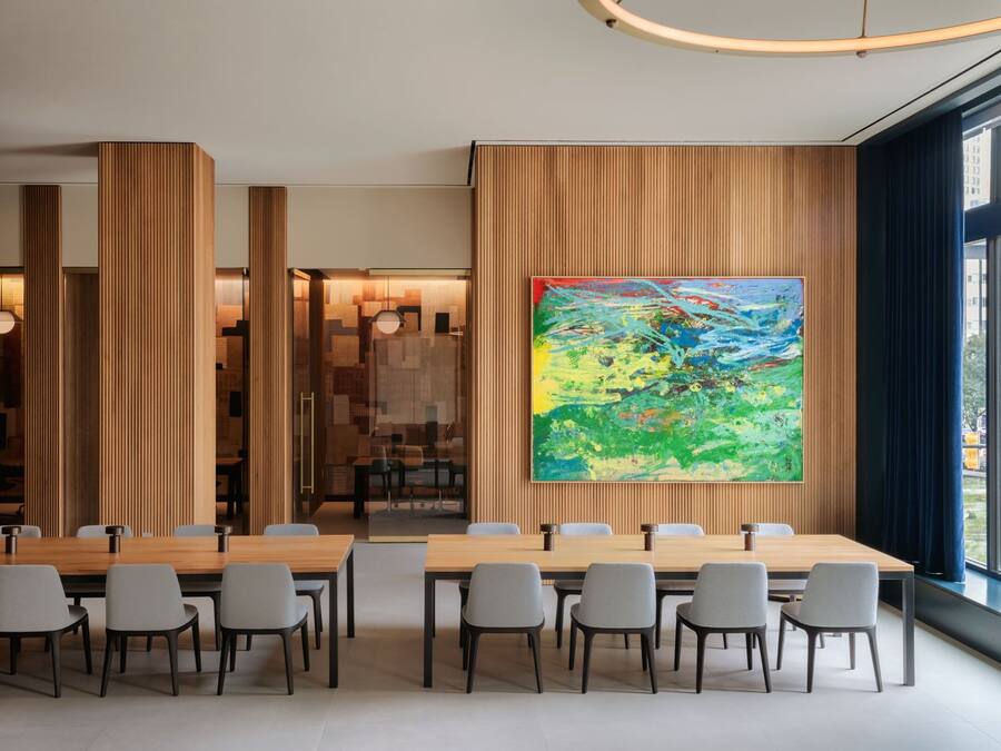 A modern conference room with a large wooden table, grey chairs, and a colorful abstract painting on the wall.