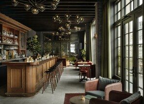 Uma área de bar com um balcão comprido, banquetas e uma adega abastecida com garrafas. Há grandes janelas e vista para o exterior.