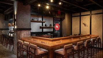 A bar area with a long wooden counter, multiple stools, and shelves with decorative items.