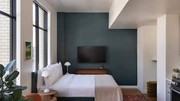 A modern hotel room with a large bed, a flat-screen TV mounted on the wall, a small table, and a chair.