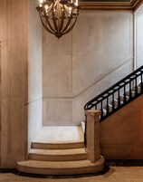 A grand staircase with a black balustrade, marble walls, and a decorative chandelier.