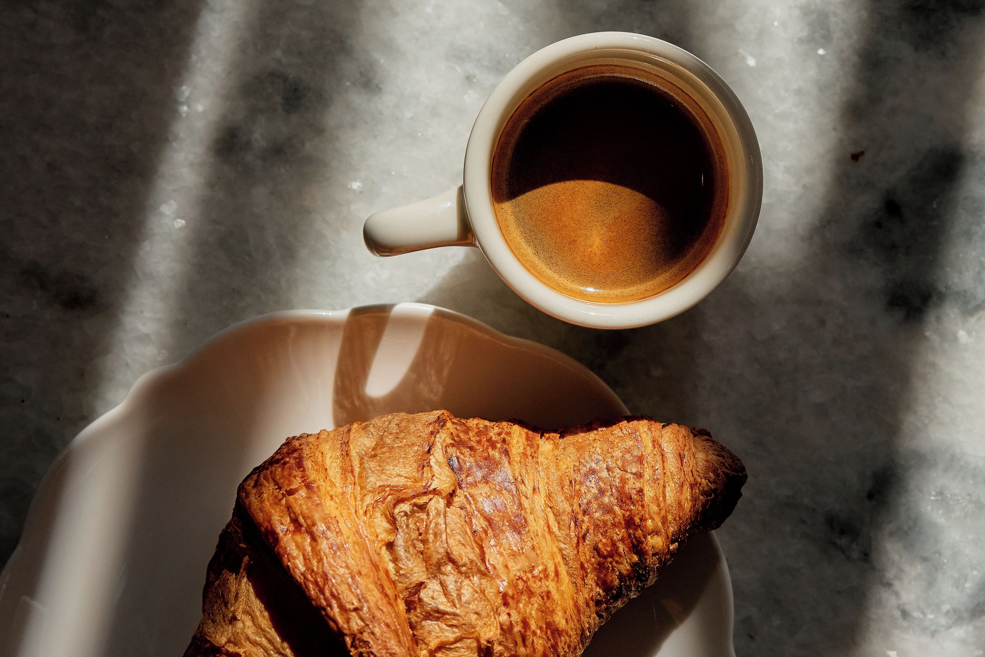 A croissant and a cup of coffee on a white plate.