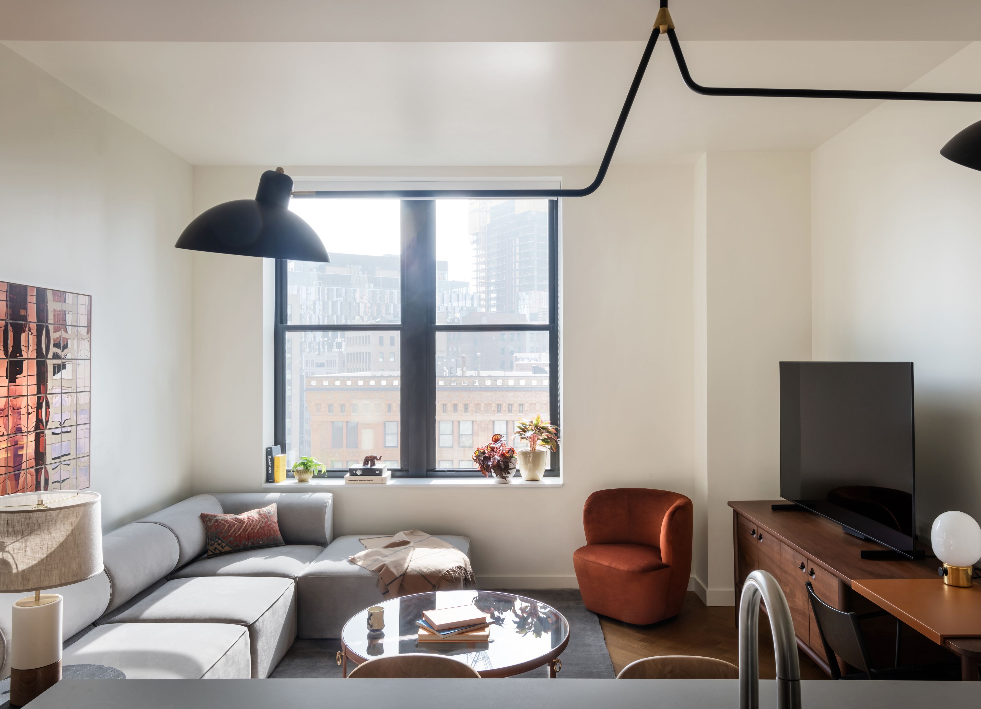 A modern living room with a large window, a sofa, a coffee table, a television, and a lamp.