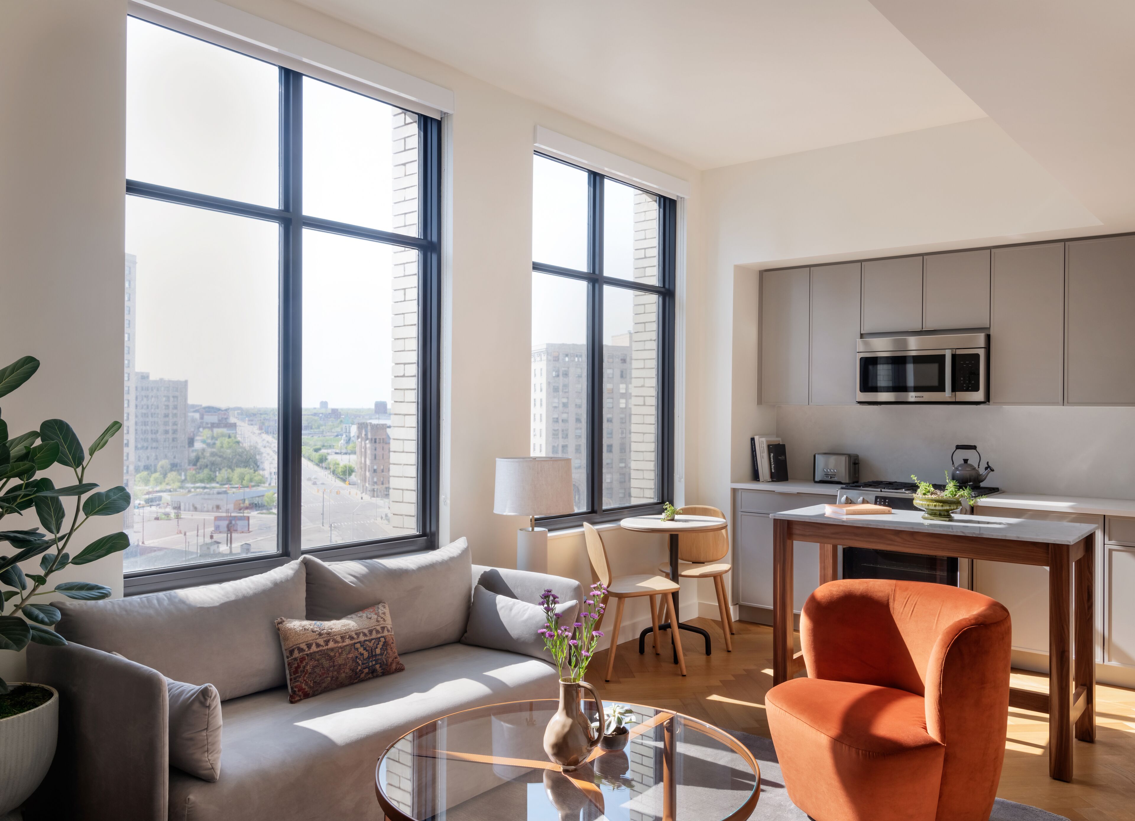 A modern apartment with large windows, a sofa, a dining table, and a kitchen area.