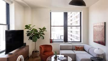 A modern living room with a flat-screen TV, a large potted plant, a red armchair, a grey sofa, and a round coffee table.