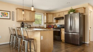Una cocina moderna con armarios de madera, electrodomésticos de acero inoxidable y una zona con taburetes de bar.