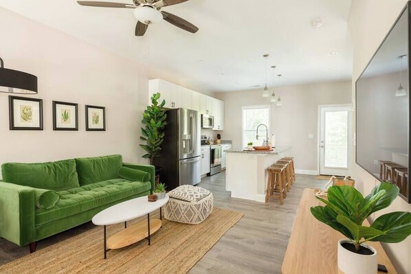 Um espaço de estar moderno com um sofá verde, uma mesa de centro e uma área de jantar com banquetas de madeira.