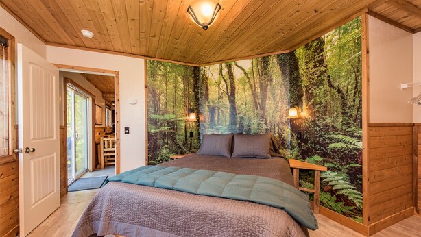 Une chambre avec un grand lit, un plafond en bois et une fresque murale sur le thème de la forêt.