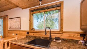 Une cuisine avec un plan de travail en bois, un évier noir et une fenêtre donnant sur les arbres.