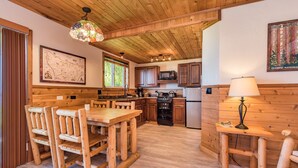 Une cuisine rustique avec des meubles de rangement en bois, un coin repas avec des chaises en bois, une cuisinière et un réfrigérateur.