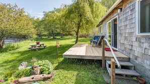 Une cabane en bois avec une terrasse, une table de pique-nique et une chaise.