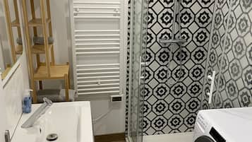Ett modernt badrum med handfat, spegel, handdukshängare, duschkabin och tvättmaskin.