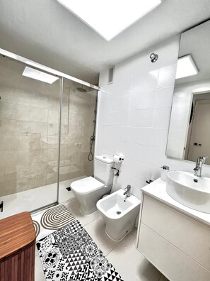 Une salle de bain moderne dotée d’une douche à parois de verre, d’un bidet, de toilettes et d’un meuble-lavabo avec un miroir.