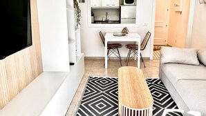 Un saló modern amb televisió de pantalla plana, un sofà, una zona de menjador amb taula i cadires, i una cuina amb armaris i microones.