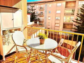 Un balcon doté de fauteuils en osier et d’une table en verre, donnant sur un quartier résidentiel avec des immeubles d’appartements.
