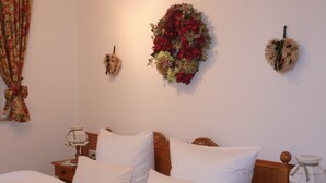 Een keurig opgemaakt bed met witte lakens en meerdere kussens, een houten hoofdbord, een nachtkastje met een lamp en een bloemendecoratie aan de muur.