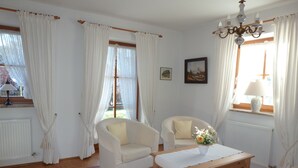 Een goed verlichte woonkamer met een bank, fauteuils, een salontafel en een kroonluchter.