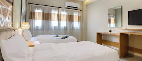 A hotel room with two beds, a desk, a TV, and an air conditioning unit.