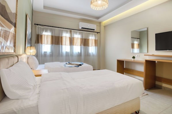 A hotel room with two beds, a desk, a TV, and an air conditioning unit.