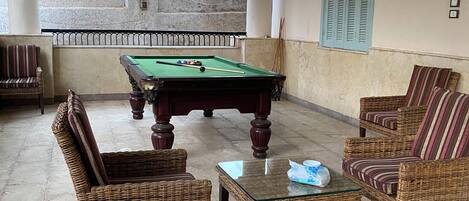 Una mesa de billar en una habitación con mobiliario de mimbre y vistas a una pared de piedra.