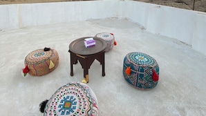 A rooftop terrace with a view of a pyramid, round tables, and colorful poufs. - Villa Khufu Pyramids Hotel (Giza)
