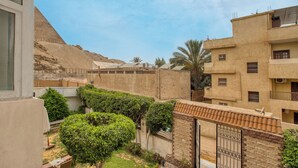 A courtyard with a view of a pyramid in the background, surrounded by buildings with balconies and a gate. - Villa Khufu Pyramids Hotel (Giza)