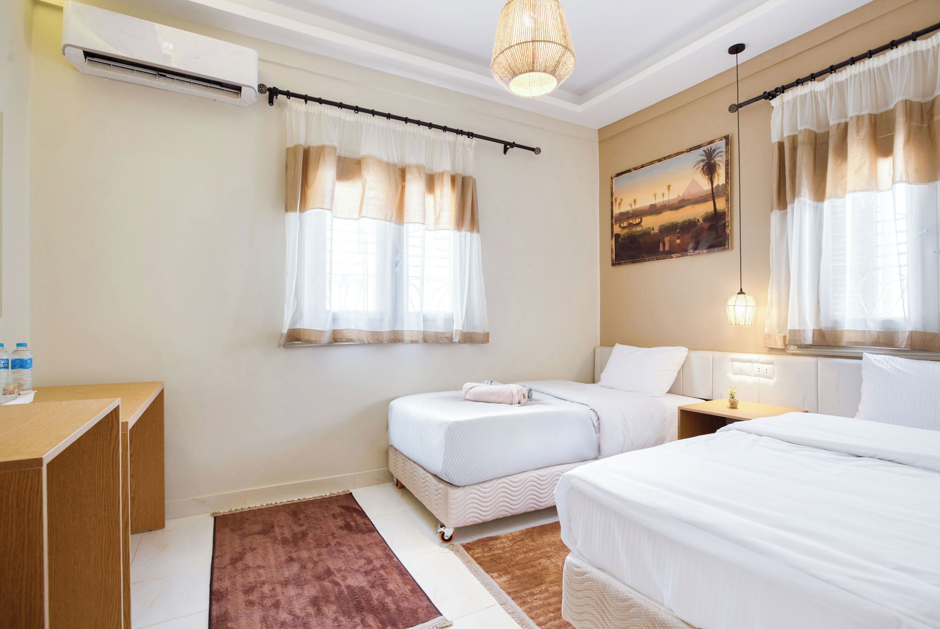 Een hotelkamer met twee bedden, een bureau, een airco, een schilderij en een raam met gordijnen.