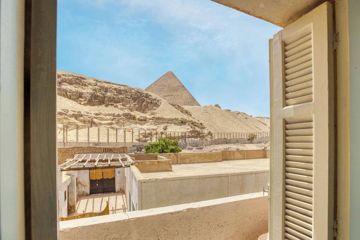 Une vue de la Grande Pyramide de Gizeh, prise à travers une fenêtre dont les stores sont baissés.