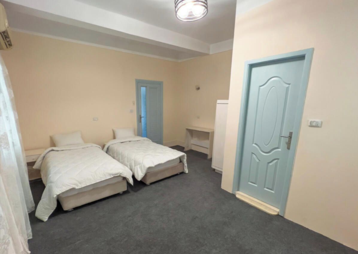 A bedroom with two beds, a door, and a desk.