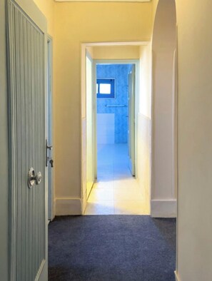 A hallway with a carpeted floor leading to a room with a window.