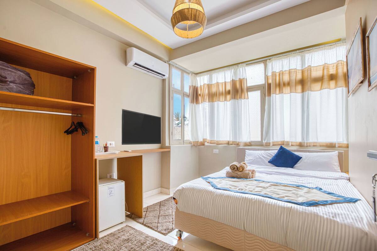 Une chambre à coucher avec un lit, une télévision, une armoire et une fenêtre avec des rideaux.