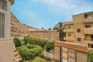 A courtyard with a view of a pyramid in the background, surrounded by buildings with balconies and a gate.