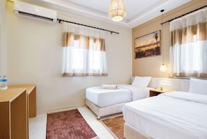 A hotel room with two beds, a desk, an air conditioning unit, a painting, and a window with curtains.