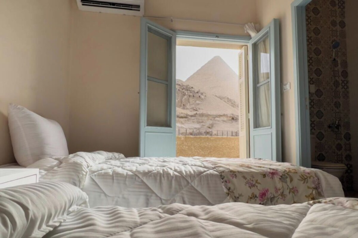 Un dormitorio con cama, mesita de noche y ventana con vista a una pirámide.