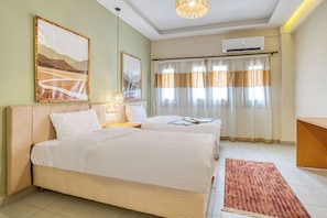 A hotel room with two beds, a large painting, a ceiling fan, and a window with curtains.