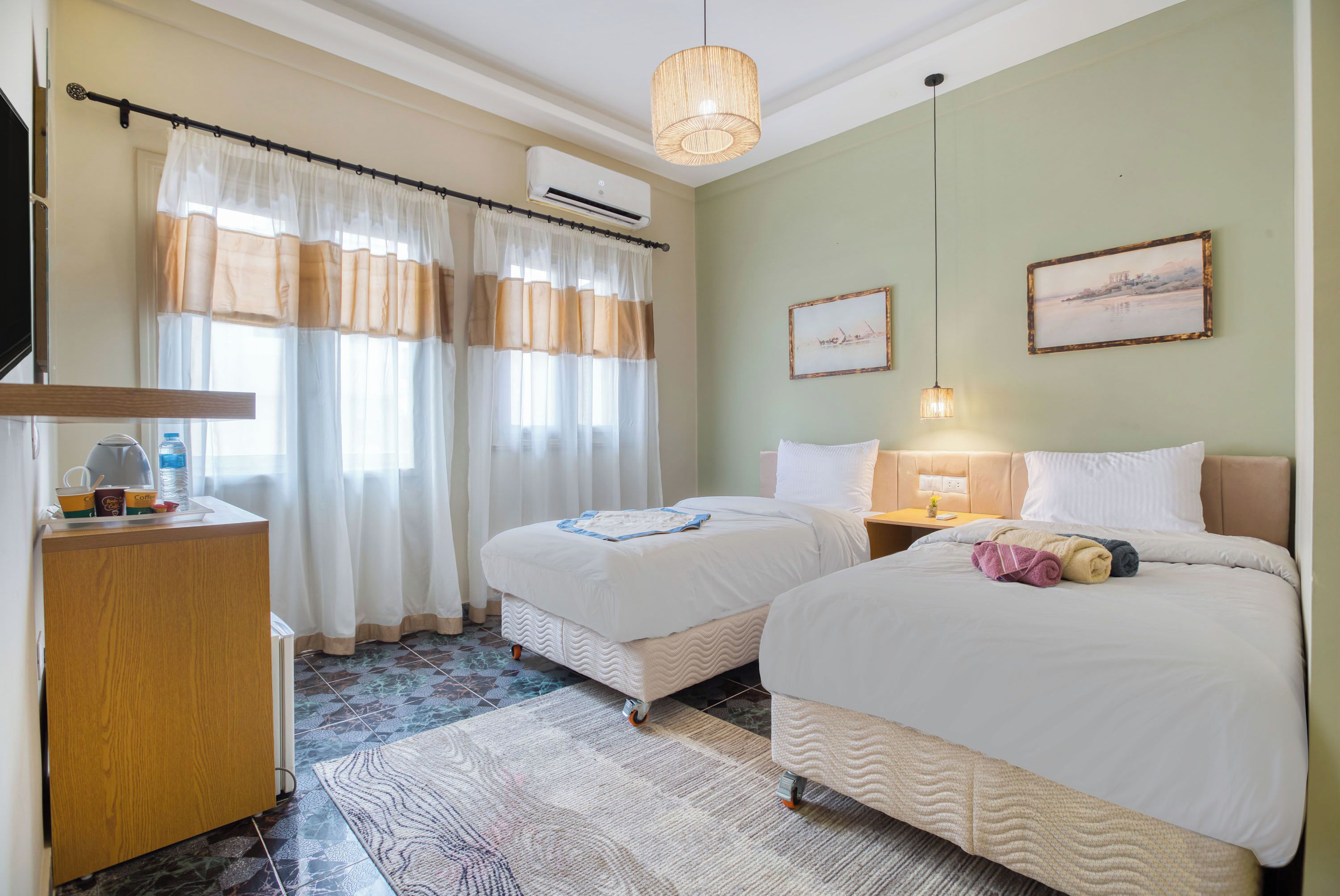 Une chambre d’hôtel avec deux lits, un bureau, une chaise, une télévision et une fenêtre avec des rideaux.